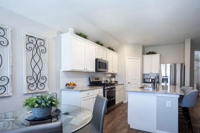 a kitchen with stainless steel appliances granite countertop a refrigerator a stove a sink and a dining table with wooden floor