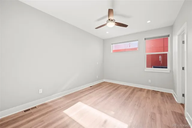 an empty room with wooden floor ceiling fan and windows