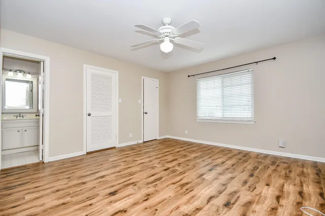 a view of an empty room with wooden floor and a ceiling fan