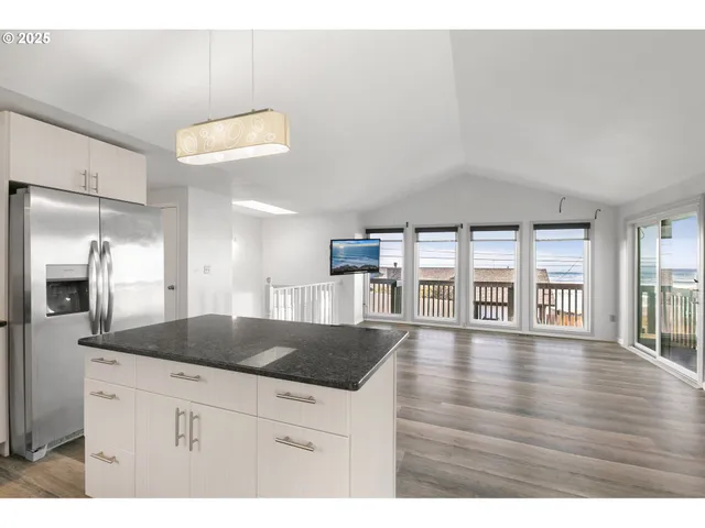 a kitchen with granite countertop a stove a refrigerator a sink and white cabinets with wooden floor