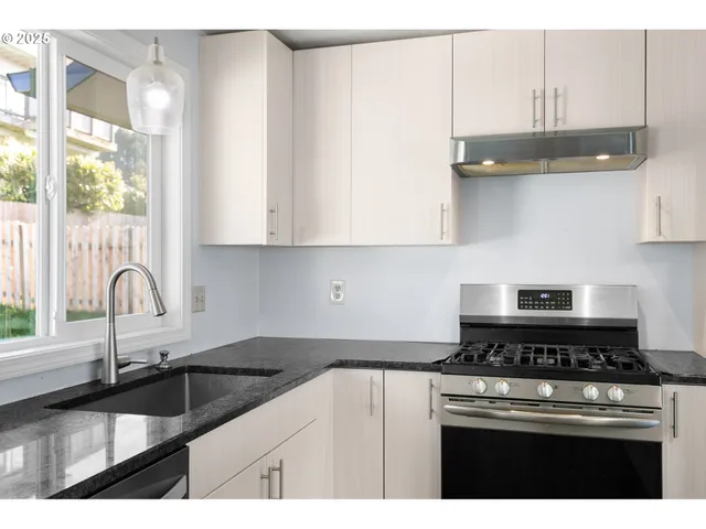a kitchen with granite countertop a sink stainless steel appliances white cabinets and a window