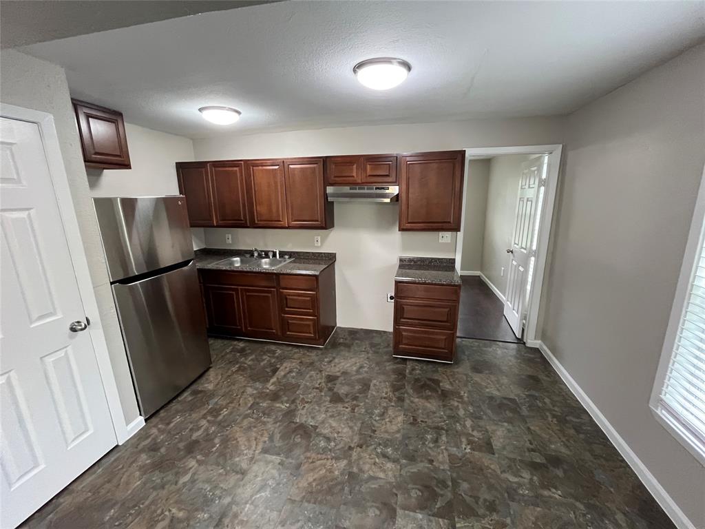 9558 Rylie Crest Drive Dallas, TX 75217 - Photo 5 of 14 Kitchen featuring dark wood-finish cabinetry, speckled countertops, stainless steel refrigerator, and range hood