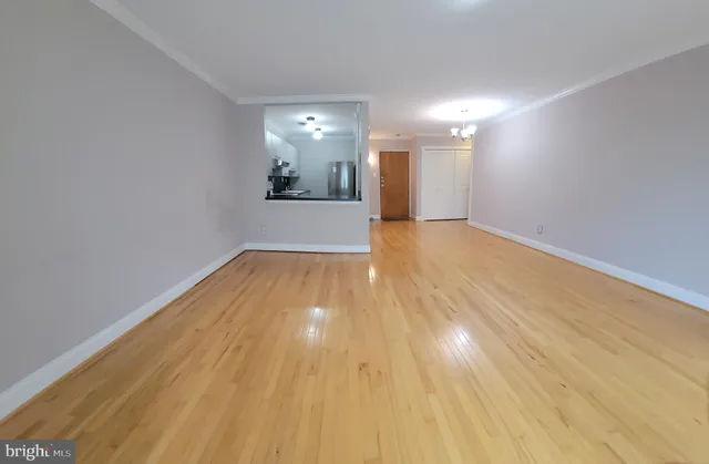 a view of empty room with wooden floor and kitchen