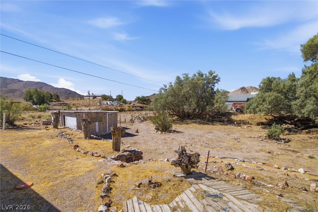 405 Main Street Beatty, NV 89003 - Photo 16 of 28 A desert landscape unfolds with scattered trees, a modest outbuilding, and distant mountains under a vast sky.