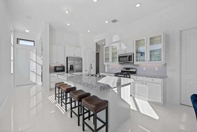 a kitchen with stainless steel appliances granite countertop a stove top oven a sink a refrigerator and white cabinets