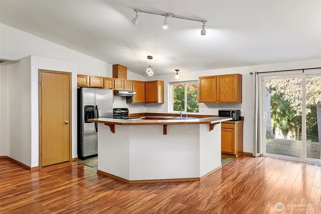 a kitchen with stainless steel appliances granite countertop a refrigerator a sink dishwasher a stove top oven a large island with wooden floor and cabinets