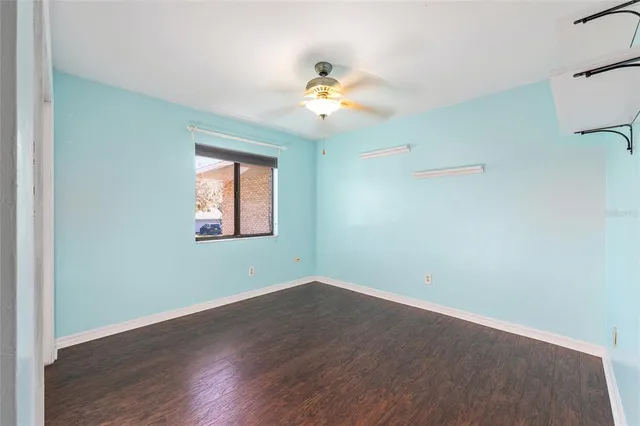 an empty room with wooden floor chandelier fan and windows