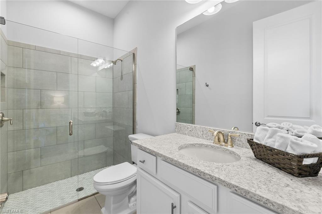 15345 Aprile Street Naples, FL 34114 - Photo 20 of 29 a bathroom with a granite countertop sink a toilet a mirror and shower