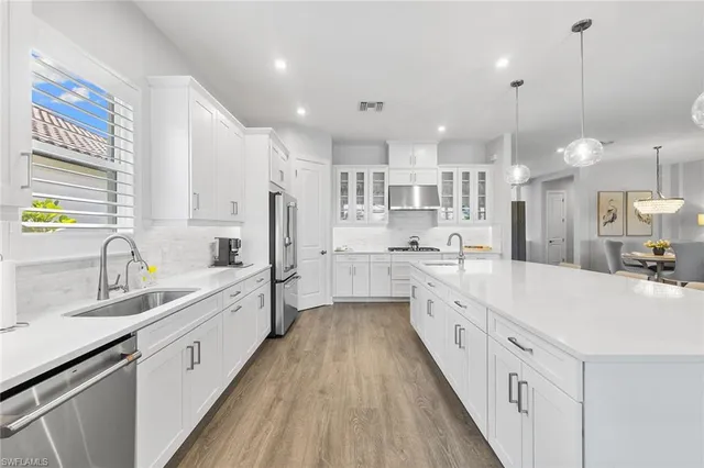 a large white kitchen with kitchen island a sink a center island stainless steel appliances and a window