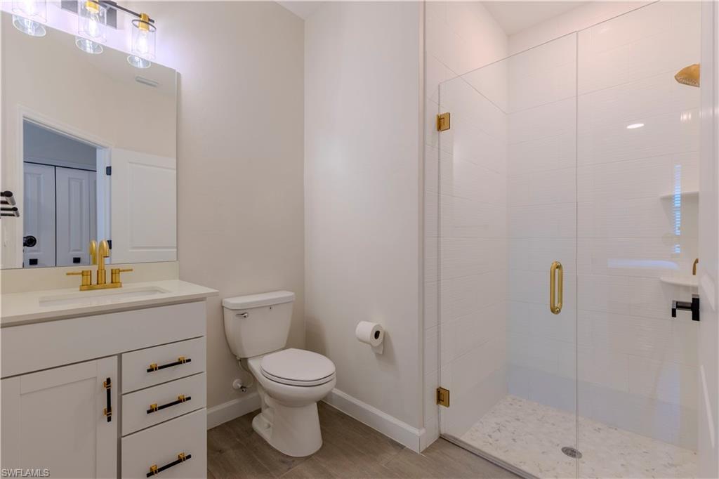 20278 Kingmont Drive Estero, FL 33928 - Photo 17 of 38 Bathroom with baseboards, toilet, vanity, wood finished floors, and a stall shower