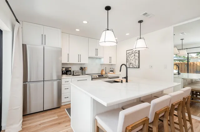 a kitchen with kitchen island a stove a refrigerator a sink a dining table and chairs with wooden floor