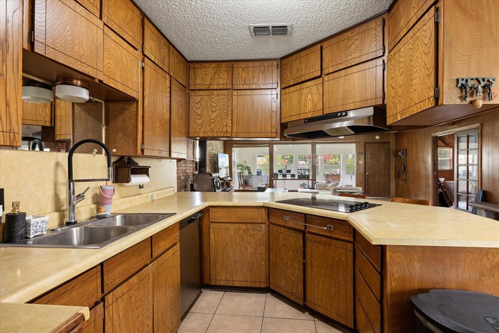 4210 Waples Road Granbury, TX 76049 - Photo 21 of 37 Kitchen featuring wood cabinetry, light-toned countertops, a stainless steel double sink, a black cooktop, and a stainless steel range hood