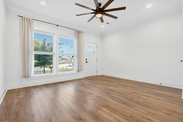 an empty room with wooden floor fan and windows