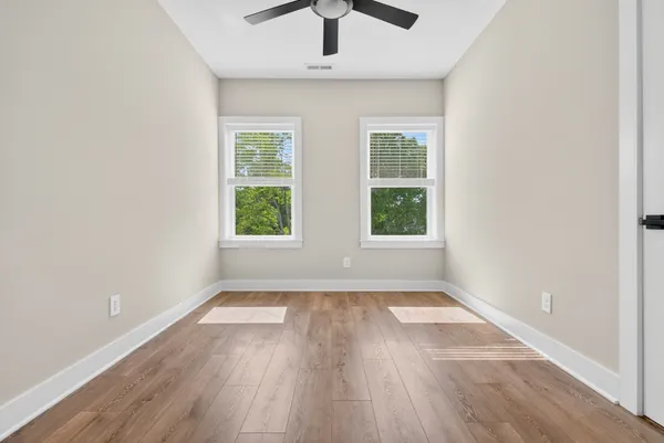 an empty room with wooden floor chandelier fan and windows