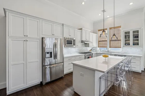 a kitchen with stainless steel appliances granite countertop a refrigerator a sink a stove and white cabinets with wooden floor