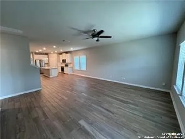 an empty room with wooden floor ceiling fan and windows