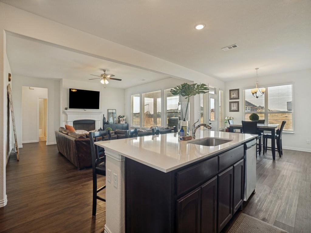 145 Prairie Trail Rhome, TX 76078 - Photo 10 of 25 Open concept layout featuring wood-finish flooring, a kitchen island with sink, a fireplace with a white mantel, and ample natural light from multiple windows