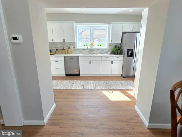 a kitchen with stainless steel appliances granite countertop a refrigerator a sink a stove and white cabinets with wooden floor