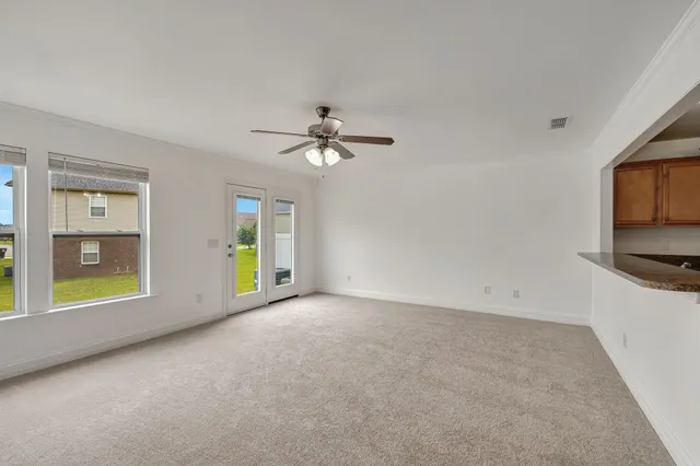 an empty room with chandelier fan and windows