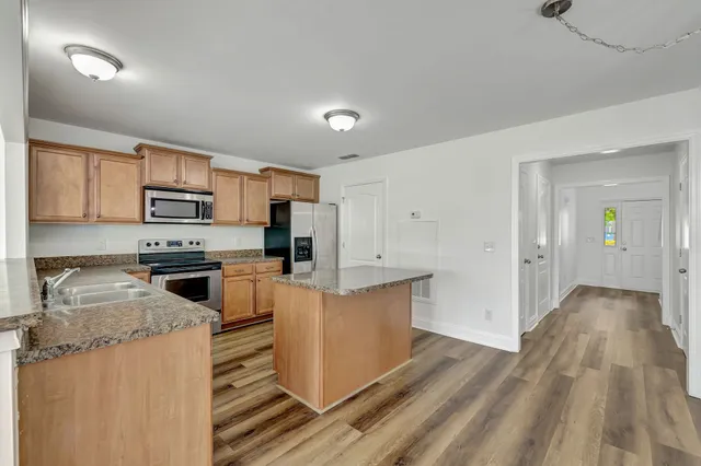 a kitchen with stainless steel appliances a stove top oven a sink a refrigerator white cabinets and wooden floor