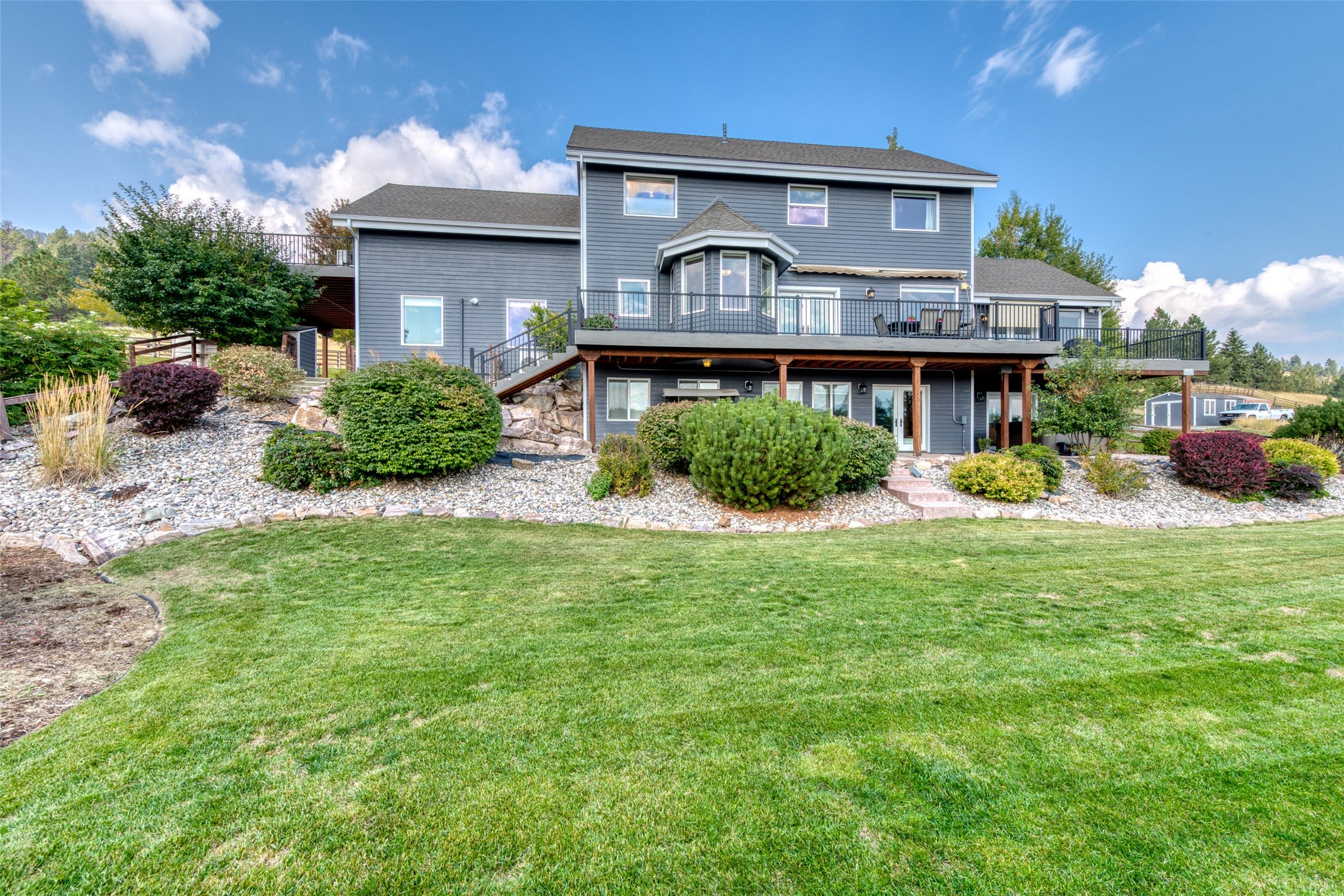 16374 Folsom Road Florence, MT 59833 - Photo 12 of 98 Rear view of house featuring a wooden deck, a lawn, and stairs