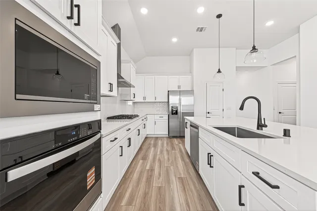 a large kitchen with stainless steel appliances a large counter top a stove a sink dishwasher and a refrigerator with wooden floor