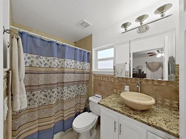 a bathroom with a granite countertop sink a toilet a mirror and shower