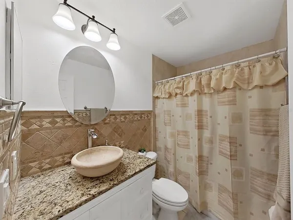 a bathroom with a granite countertop sink a toilet a mirror and shower curtain