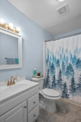 a bathroom with a granite countertop toilet a sink a mirror and a shower