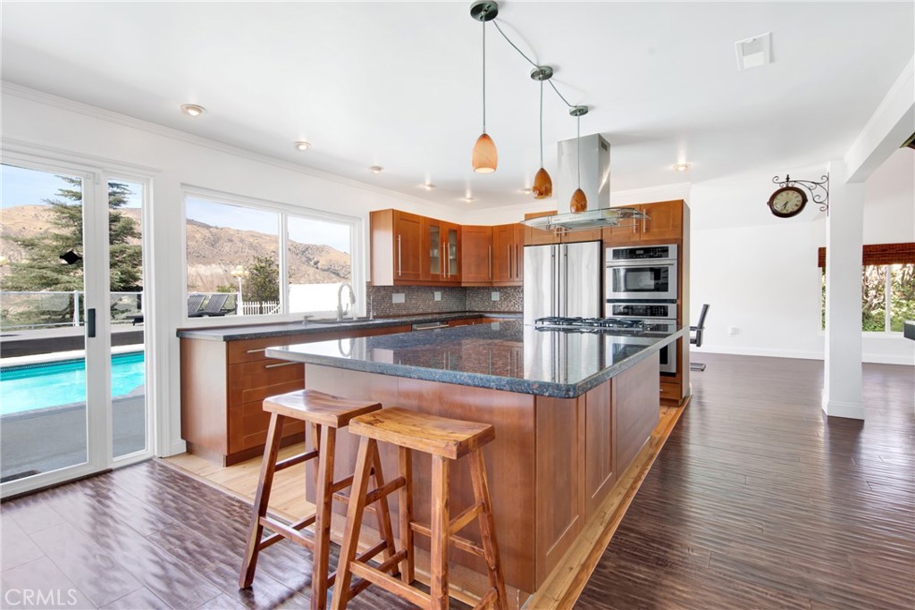 12036 Darby Avenue Porter Ranch, CA 91326 - Photo 20 of 37 a kitchen with stainless steel appliances kitchen island granite countertop a table chairs in it and wooden floors