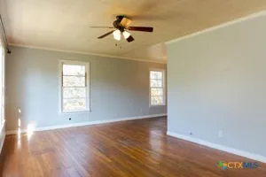 an empty room with wooden floor chandelier fan and windows