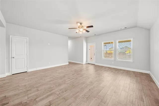 an empty room with wooden floor ceiling fan and windows