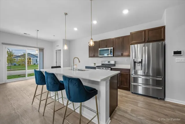 a kitchen with stainless steel appliances a sink a stove a refrigerator and island with wooden floor