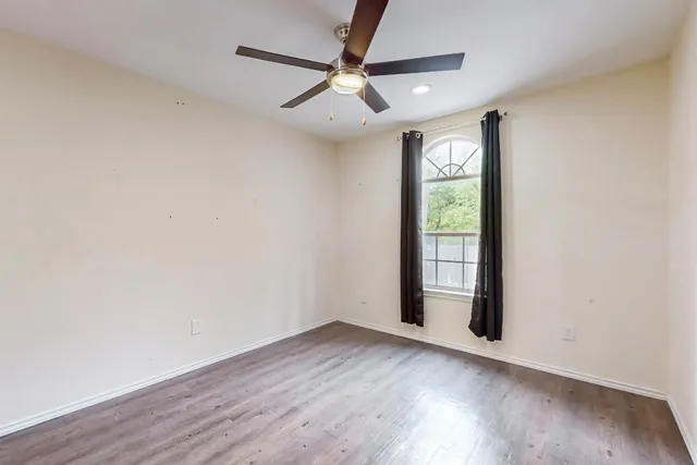 an empty room with wooden floor fan and windows