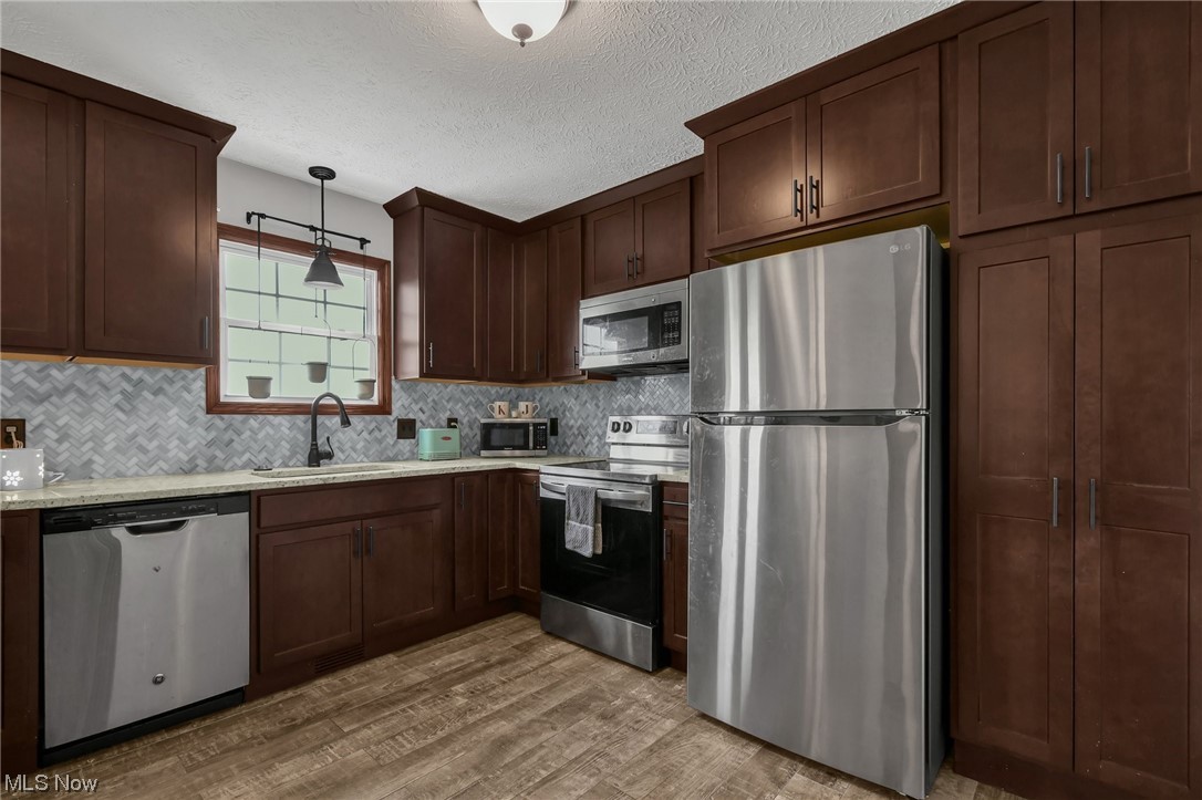 681 Rocky Point Road Fleming, OH 45729 - Photo 8 of 33 Kitchen featuring appliances with stainless steel finishes, a textured ceiling, dark brown cabinetry, light countertops, backsplash, and light hardwood floors