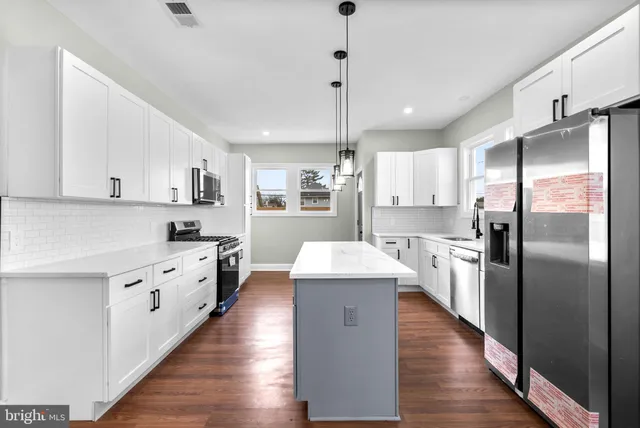 a large kitchen with stainless steel appliances a refrigerator a sink dishwasher a oven and white cabinets with wooden floor