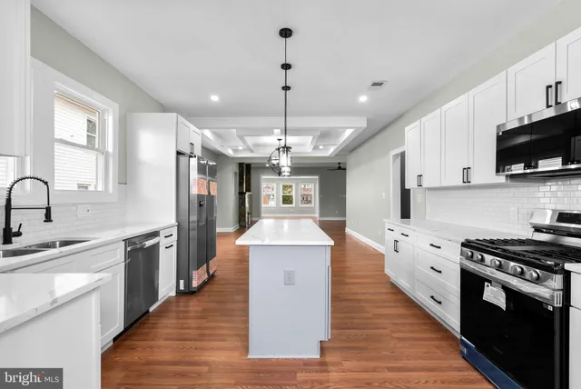 a large kitchen with stainless steel appliances kitchen island granite countertop a stove top oven a sink dishwasher a refrigerator and white cabinets with wooden floor