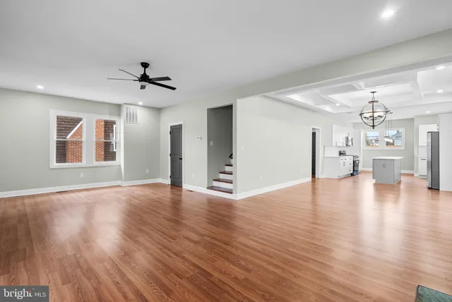 a view of an empty room with wooden floor and a kitchen