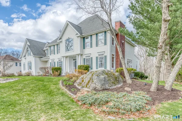 a view of a white house next to a yard with large trees
