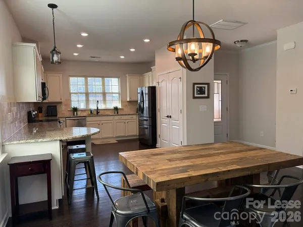 a kitchen with stainless steel appliances granite countertop a stove a refrigerator a sink a dining table and chairs with wooden floor