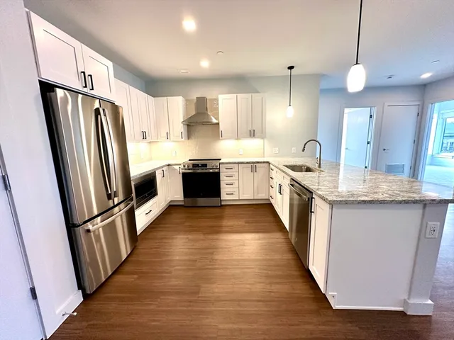 a large kitchen with granite countertop a refrigerator a sink dishwasher a stove and white cabinets with wooden floor