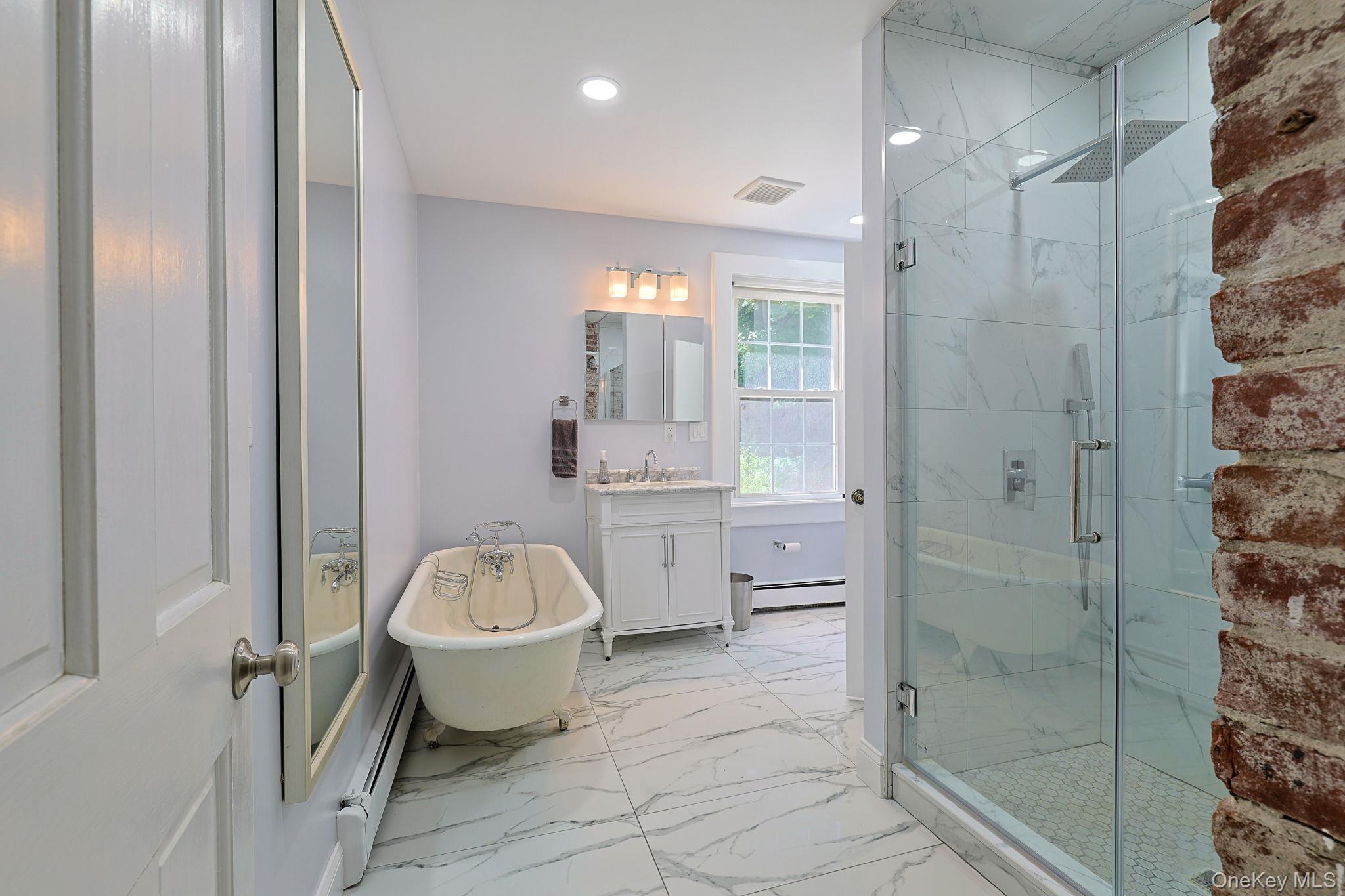 9 Library Road Tuxedo Park, NY 10987 - Photo 14 of 37 Bathroom featuring a glass-enclosed shower with rainfall showerhead, white marble-style tile, freestanding clawfoot bathtub, and a single vanity with a white countertop
