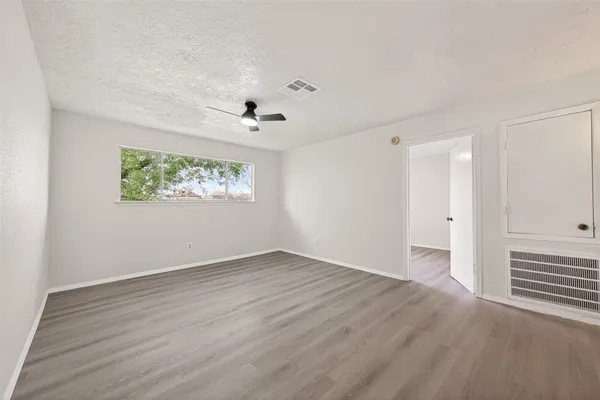 a view of an empty room with wooden floor and a ceiling fan