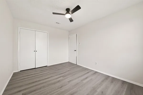 an empty room with wooden floor ceiling fan and windows