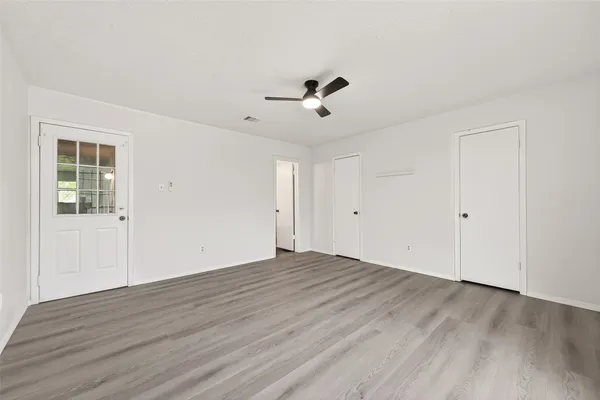 an empty room with wooden floor a ceiling fan and windows