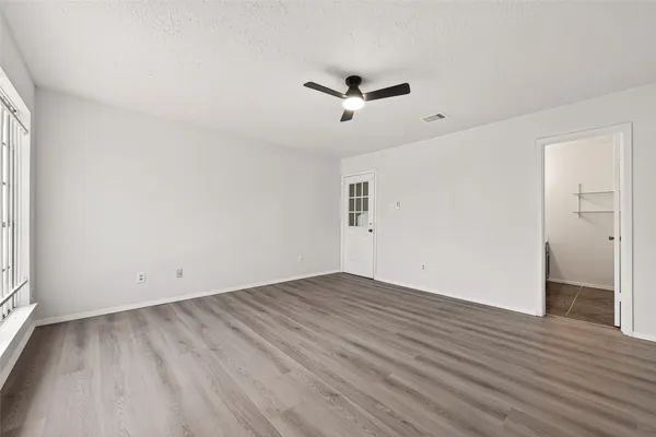 an empty room with wooden floor fan and windows