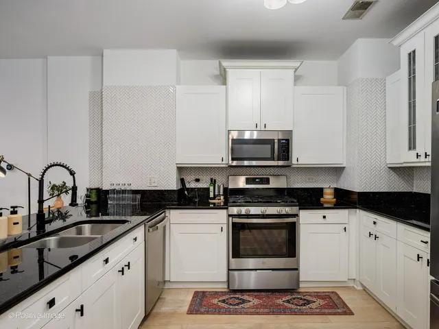 a kitchen with granite countertop a stove a sink and white cabinets