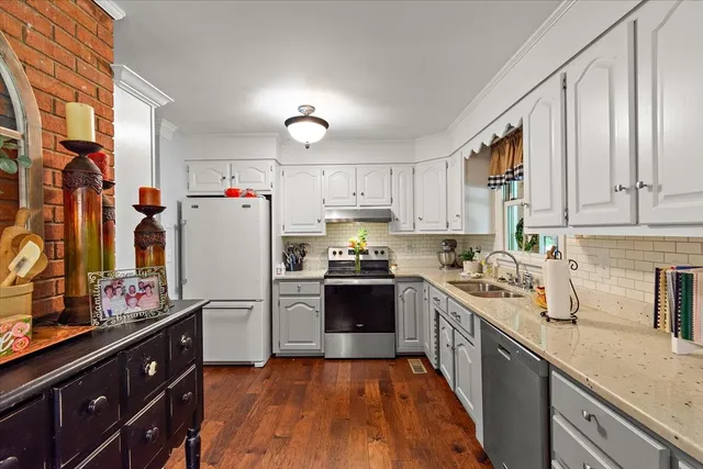 a kitchen with granite countertop a refrigerator a sink dishwasher and a stove with wooden floor