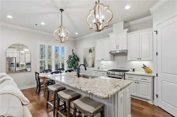 a kitchen with stainless steel appliances granite countertop a stove top oven a refrigerator a sink and couches with wooden floor