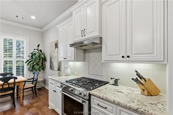 a kitchen with granite countertop a stove a sink dishwasher and white cabinets with wooden floor
